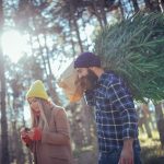 An image portraying a cheerful young couple using their afternoon to enjoy the woods and find a Christmas tree. They've found cute acorns too.